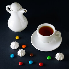 Obraz na płótnie Canvas Tea in a porcelain cup, teapot and sweets on a black .