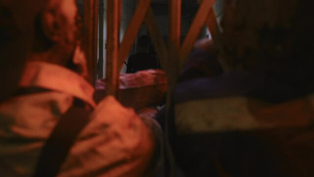 Caucasian woman with shaved head standing in dark creepy building, looking at three zombies stuck behind metal gate of old elevator reaching their hands out, hunter walking away