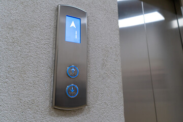 Close-up of the elevator call button up and down with braille. Arrow shows the lift going up