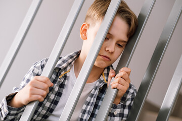 A young guy with an angry or offended expression is holding on to the railing bars.