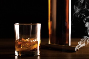 Man's cigar, elegant glass of brandy on the bar counter. Alcoholic drinks, cognac, whiskey, port, brandy, rum, scotch, bourbon. Vintage wooden table in a pub at night.