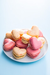 Heart shaped Sweet macarons on plate on blue table.