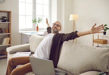 Happy adult man who has finished his work is sitting on sofa at home with notebook and laptop...