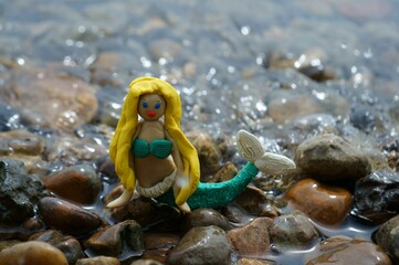 A mermaid figurine on the river bank. A fairy-tale character. A toy mermaid. Female appearance.