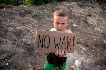 A boy with a grimy face and sad eyes holds a cardboard poster with the inscription NO WAR