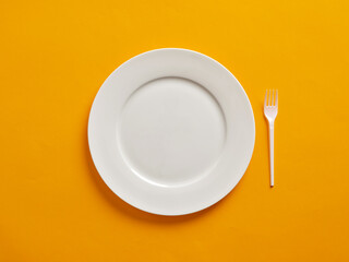 Empty or blank white plate with plastic fork on yellow background.