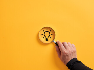 Hand holding a magnifier over the idea light bulb icon. To search, find or focus on an idea