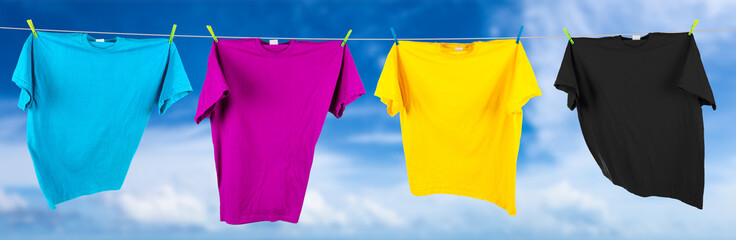 Colorful CMYK colored t-shirts on clothes line in front blue sky summer background. Cyan magenta...