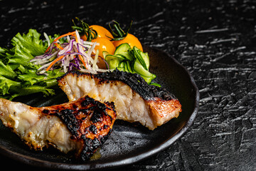 Grilled tilefish marinated with saikyo-miso and tomato salad on a black plate against a black design board.