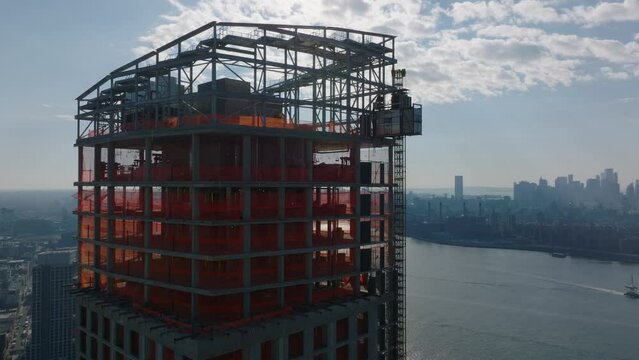 Aerial view of upper section of high rise building under construction against sky with bright clouds. New York City, USA