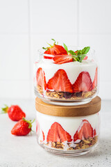 Strawberry parfait with yogurt and granola in glass jar. Healthy breakfast recipe. Summer dessert concept.