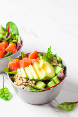 Hawaiian poke - brown rice, salmon, edamame, cucumber and avocado in gray bowl, marble background. Fish fresh salad for a healthy diet.