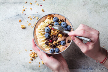 Chocolate banana smoothie bowl with granola, berries and hemp seeds, gray background. Healthy vegan...