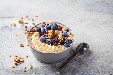 Chocolate banana smoothie bowl with granola, berries and hemp seeds, gray background. Healthy vegan recipe concept.