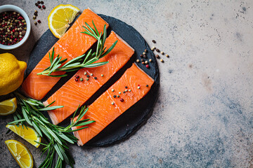 Pieces of raw salmon with spices and herbs on slate board, dark background.