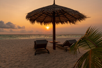 Beach chairs and straw umbrella during sunset