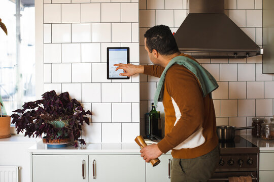 Side view of man using home automation device on wall while standing in kitchen at home