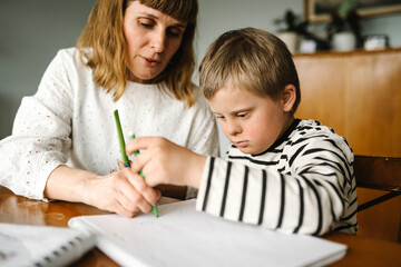Boy with disability taking support of mother while drawing in book at home