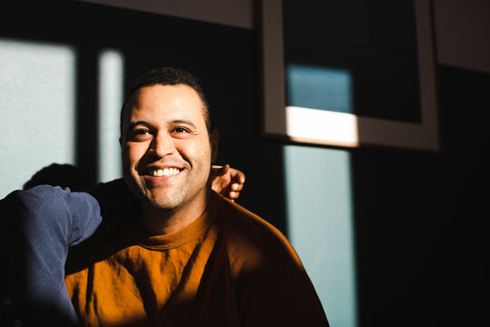 Smiling man with son contemplating against wall during sunny day