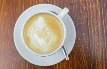 There is a cup of coffee on a wooden brown table during the day