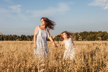 Young mother and daughter dance in field.