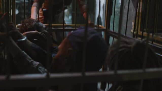 Military woman with shaved head dragging away creepy zombies in cage on wheels in dark basement of industrial building
