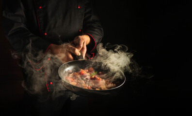 Cooking vegetables on a hot frying pan in the hands of a chef. Molecular gastronomy or cuisine