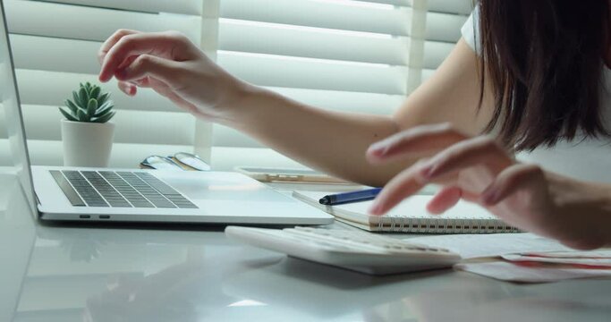 Young woman calculating monthly home expenses, tax, credit card bills payment and bank account balance in living room at home. Managing budget, entering data in computer application.