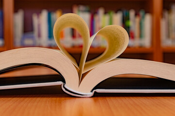 Close-up of an open book with its pages in the shape of a heart, on the table of a reading room in...