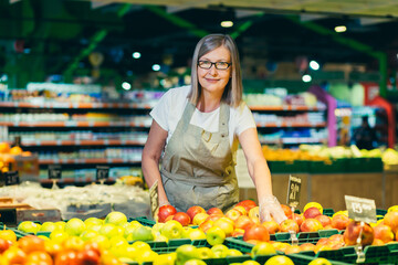 Portrait of senior woman in glasses at grocery store employee, supermarket. Stands in work clothes,...