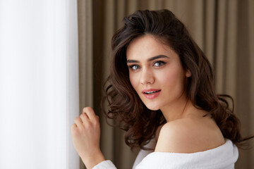 Naklejka premium Smiling brunette young woman with hairstyle in a white bathrobe after beauty procedures.