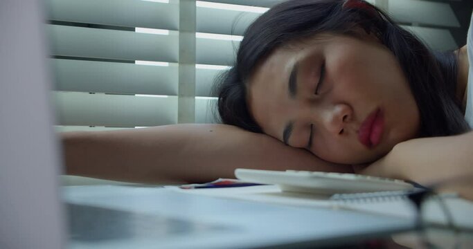 Slow motion and close up of overworked and tired businesswoman Asian sleeping on her desk and leaning on her arm at home office.Modern problems and issues with working from home.