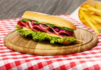 Philly cheesesteak sandwich made with cheese and onions with french fries on a wooden board
