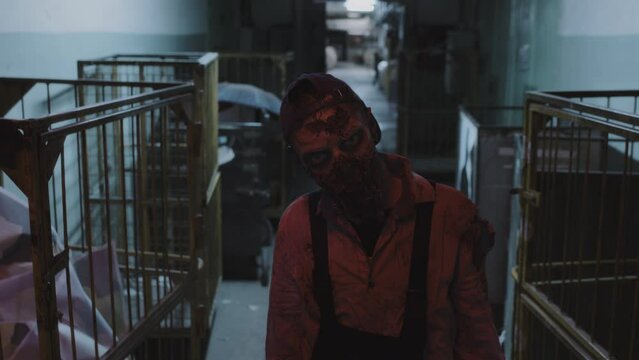 High angle waist-up of male evil zombie twitching in creepy basement with lights flashing in industrial building