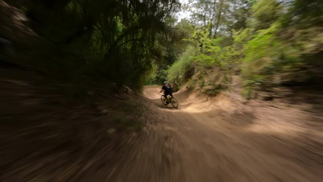 Mountain-bike rider riding fast at forest Trail Pathan followed by fpv drone 