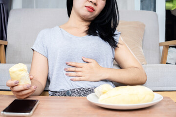 Asian woman having  stomachache overeating durian, indigestion because of acid reflux, hand holding...