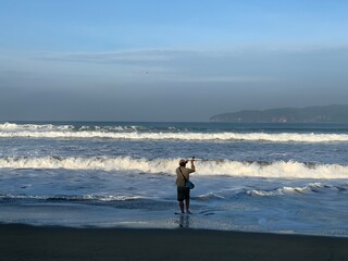 Fisherman fishing at the beach with waves in front of him