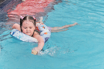 Happy adorable Asian little girl swims in inflatable circle, having fun in open air thermal pool.