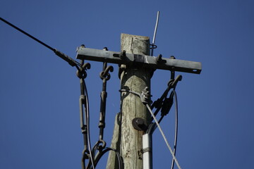 Fototapeta na wymiar Wires and top of old wooden telegraph pole plus small cobbweb on the right side under a blue spring sky, concept: vintage, use: background, wallpaper, copy space (horizontal), Sehnde, Germany
