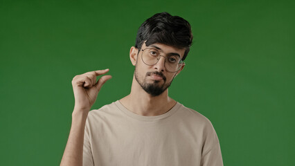 Disappointed unhappy brunette arabian man make little bit gesture with fingers dissatisfied guy show small size shape low rating measuring inch tiny scale standing isolated indoor on green background