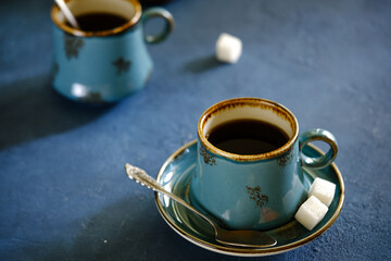 A crispy croissant with almond filling and hot black coffee on a wooden board on a blue concrete table.