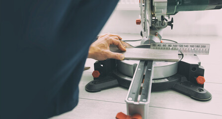 A worker cuts a skirting board made of fibreboard with a miter saw