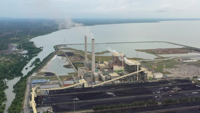 Drone fly around coastal coalfield, industrial ultra-supercritical coal-fired power plant with smokes raising from chimney located at lekir bulk terminal jalan, teluk rubiah, manjung, perak, malaysia.