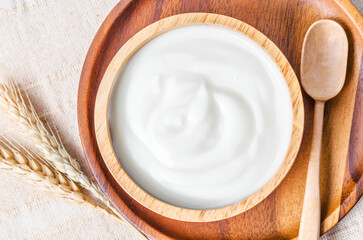 Greek yogurt in a wooden bowl and dry barley on table.
