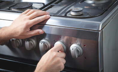 Male hand turning switch knob on gas stove.