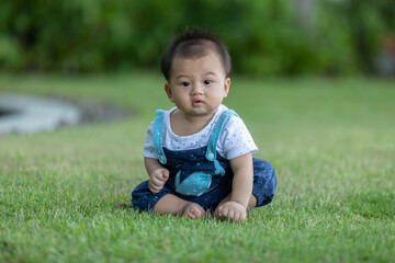 Adorable asian baby sit on green grass spend time to learn be all around. First time to touch grass of cute baby infant excite and happiness. Little baby boy playing outdoor and looking at camera