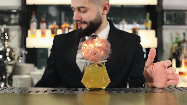 Professional bartender wearing stylish black suit using gas burner to set on fire steel wool that decorating unique alcoholic drink. Creative and fancy preparation of cocktail at luxury restaurant.