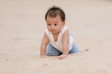 Healthy asian baby toddler crawling on the beach to learn to crawl outdoors. Adorable baby keeping her belly and legs down on sand to belly crawl fun and happiness at home. Baby growth concept