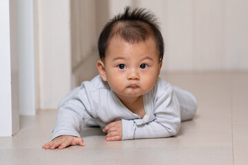 Healthy asian baby toddler crawling on floor to learn to crawl indoors. Adorable baby keeping her belly and legs down on the floor to belly crawl fun and happiness at home