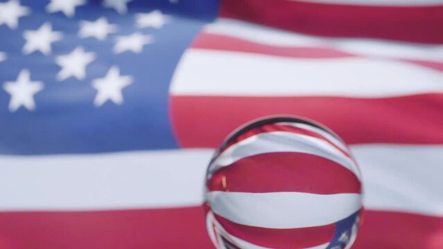 American flag is waving at a beautiful and peaceful sky in day while camera passes in front of a glass ball with dolly shot.